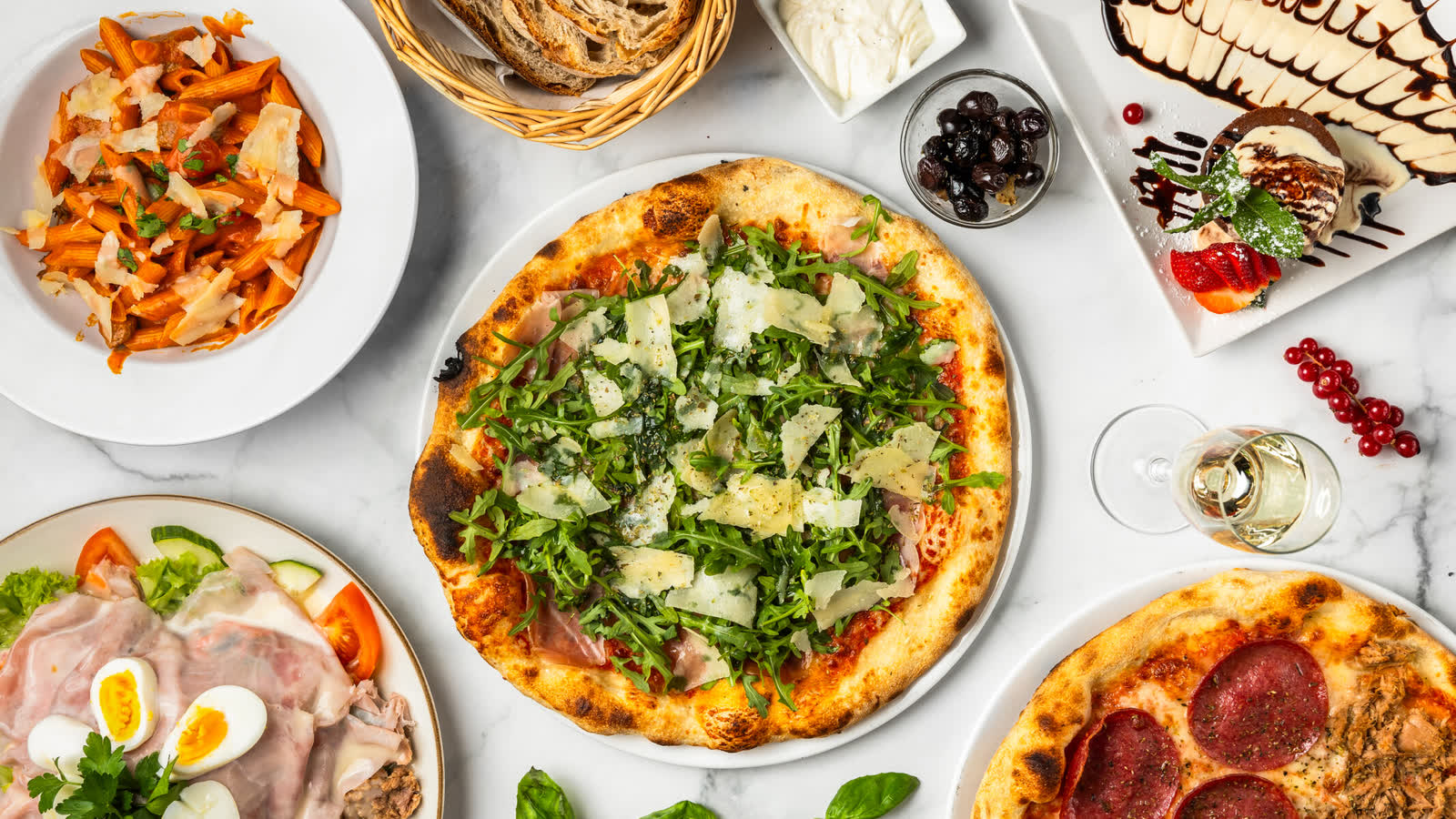 Pizza met rucola en Parmezaanse kaas, met daaromheen pasta, salade, brood en een pepperonipizza.